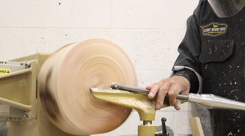 artist holding a piece of wood against a machine that's carving it into a table leg